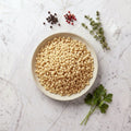 Overhead view of a bowl of TK Farfel, small toasted pasta pellets, on a marble surface