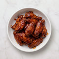 Overhead view of a bowl of TK Pre-Cooked Chicken Wings coated in glossy BBQ sauce
