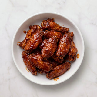 Overhead view of a bowl of TK Pre-Cooked Chicken Wings coated in glossy BBQ sauce