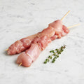 Two raw chicken shishkebob skewers on a white marble surface