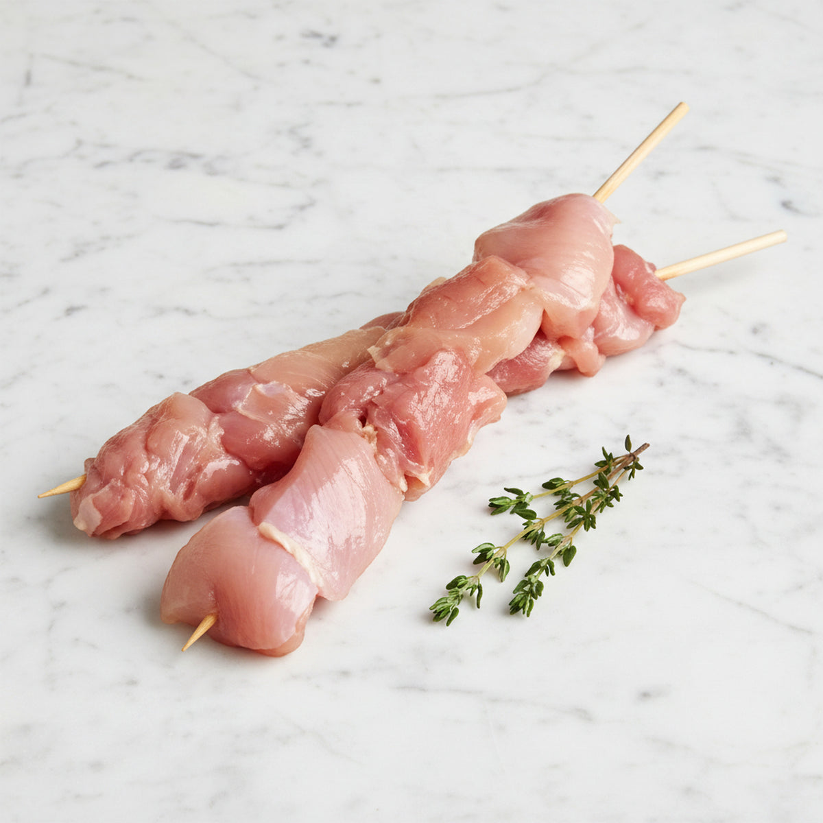 Two raw chicken shishkebob skewers on a white marble surface