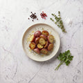 Overhead view of TK Red Skin Roasted Potatoes, halved and herbed, on a speckled plate