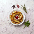 Overhead view of TK Roasted Potato Wedges arranged around a dish of ketchup on a marble surface