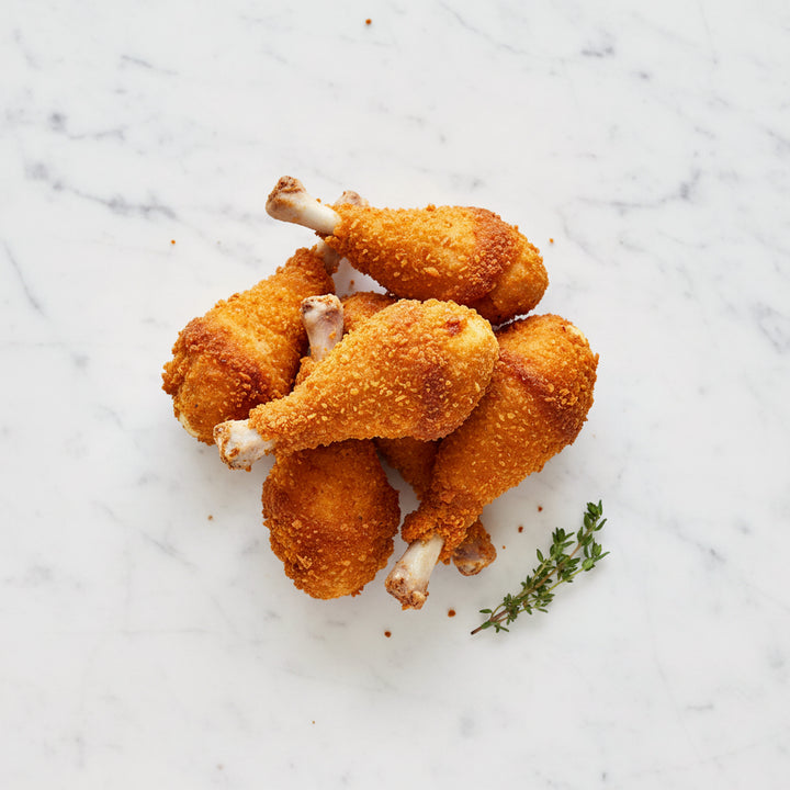 Breaded chicken drumsticks on a white marble surface