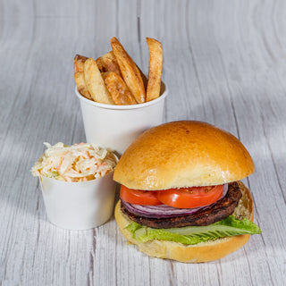 Beef burger with tomato, red onion and lettuce, with a cup of fries and coleslaw on a wooden table