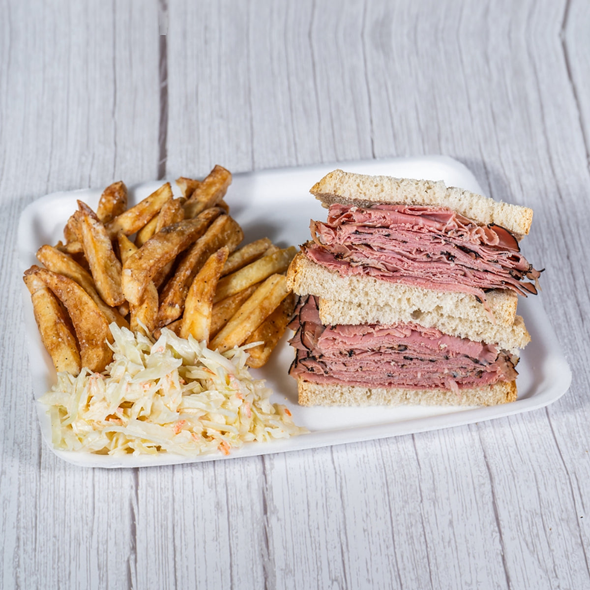 Beef pastrami sandwich on rye with fries and coleslaw on a white tray