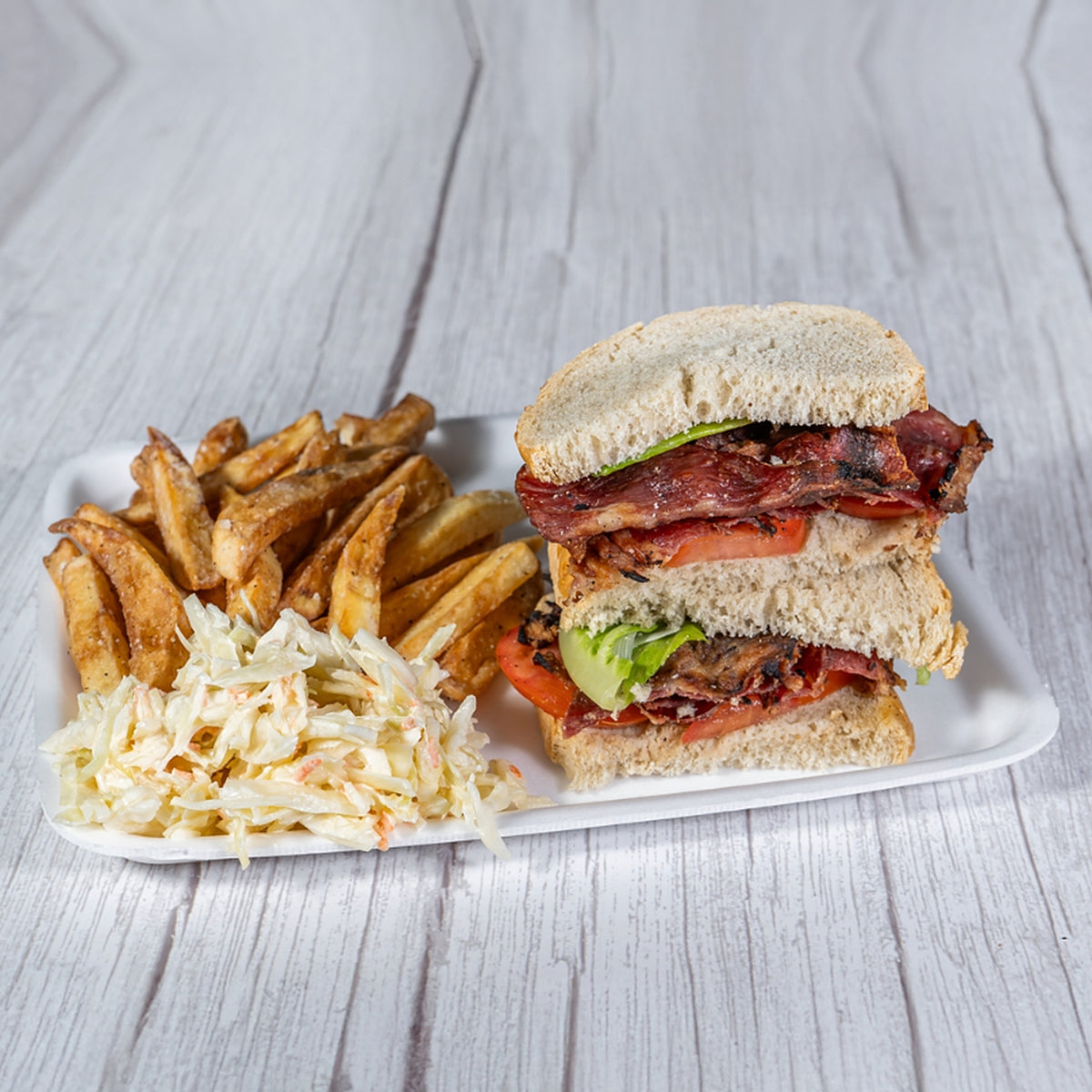 BLT sandwich on rye with fries and coleslaw on a white tray