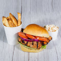 Grilled chicken breast on a bun with tomato, red onion and lettuce, with fries and coleslaw on a wooden table