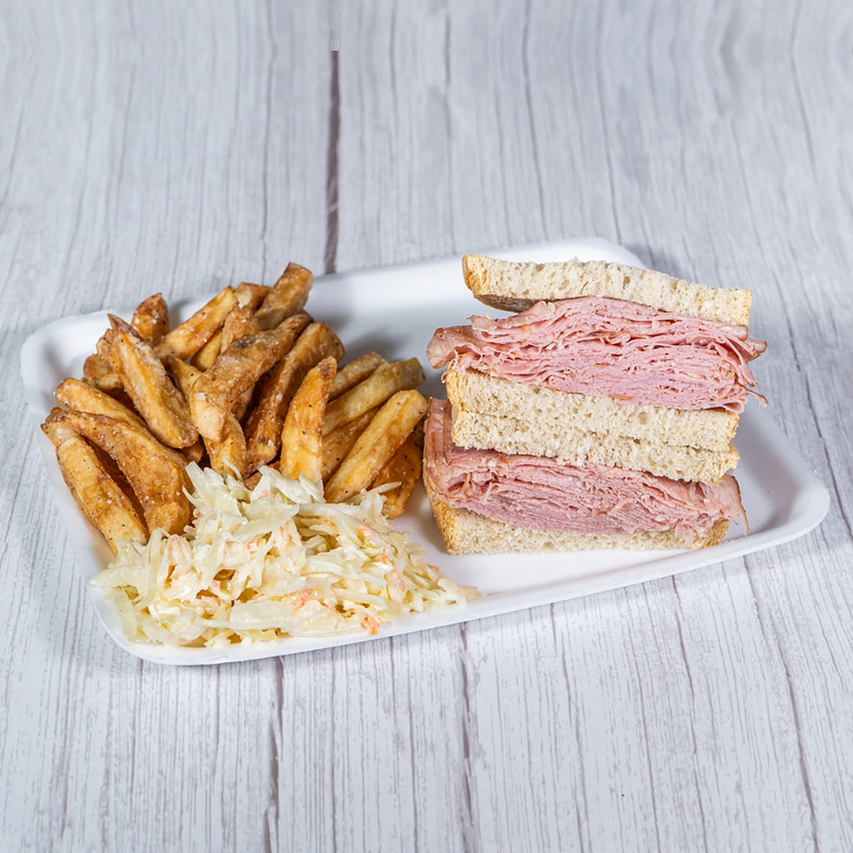 Corned beef sandwich on rye with fries and coleslaw on a white tray