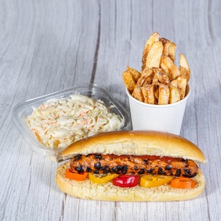 Grilled hot dog with mini peppers in a bun, with coleslaw and a cup of fries on a wooden table