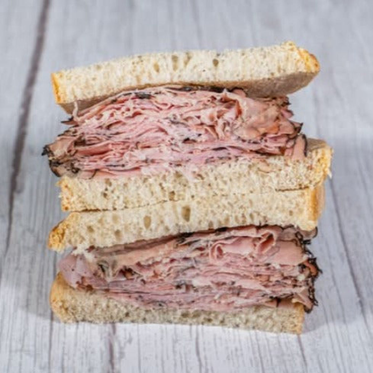 Montreal smoked meat sandwich on rye, cut and stacked, on a wooden table