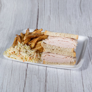 Sliced turkey roll sandwich on rye with fries and coleslaw on a white tray