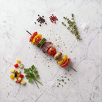 Overhead view of a Vegetable Shishkebob skewer with peppers, zucchini, tomato, mushroom and red onion on marble